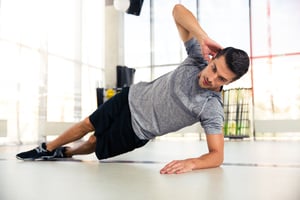 Portrait of a handsome man doing side plank at gym