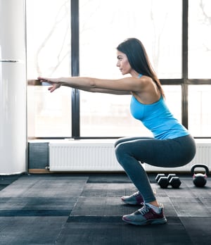 Side view portrait of a young woman doing squats at fitness gym